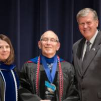 Provost, faculty member and President Emeritus Haas smile for a photo on stage.